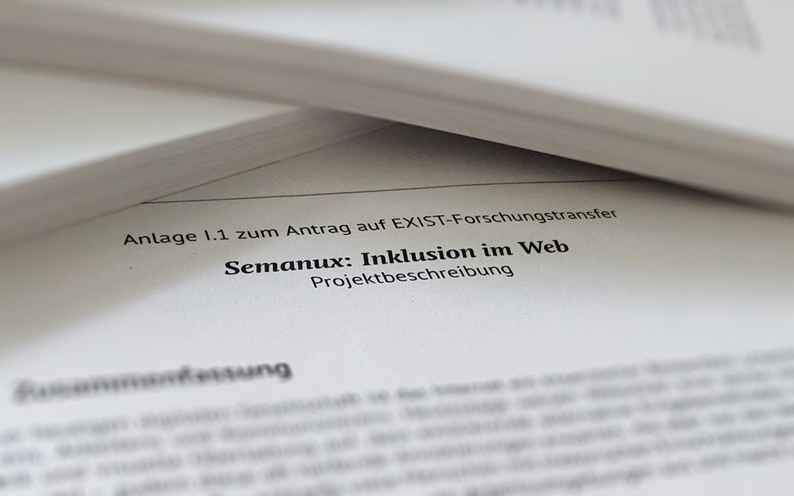 Closeup of a document showing the headline "Anlage I.1 zum Antrag auf EXIST-Forschungstransfer. Semanux: Inklusion im Web. Projektbeschreibung."